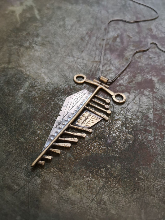 A sterling silver and brass necklace with a pendant featuring a design that resembles an arrow, attached to a chain.