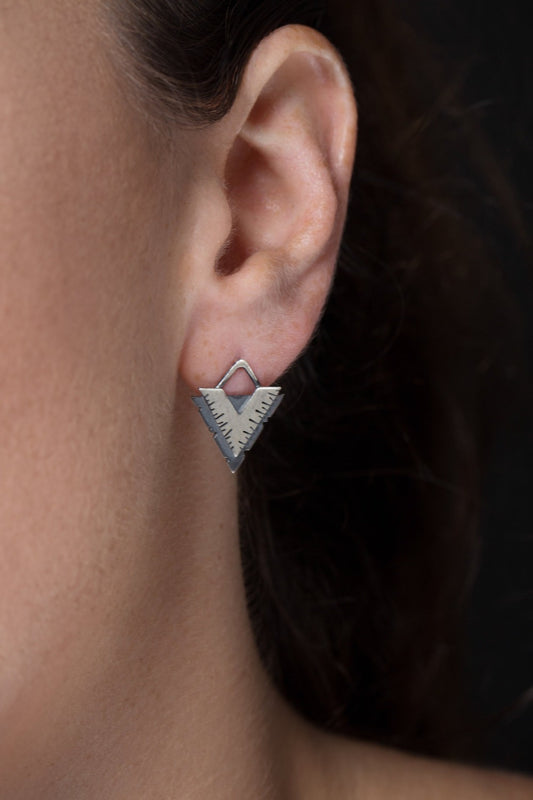 A pair of silver earrings with a geometric design, featuring a triangular shape with lines on the side