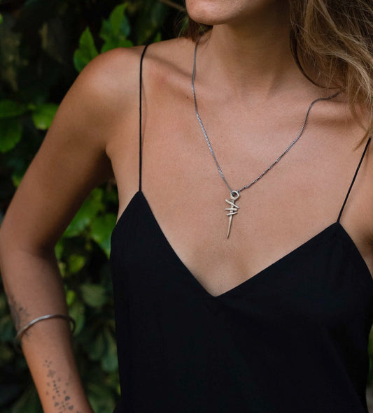 A silver necklace with a pendant featuring a symbol, attached to a chain.