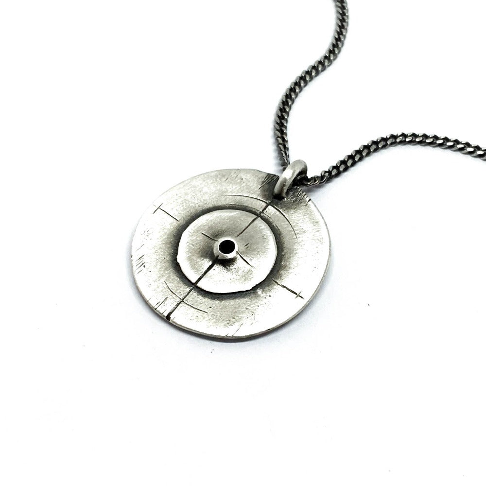 A silver necklace with a pendant featuring a circular design and a chain that ends in a pendant loop.