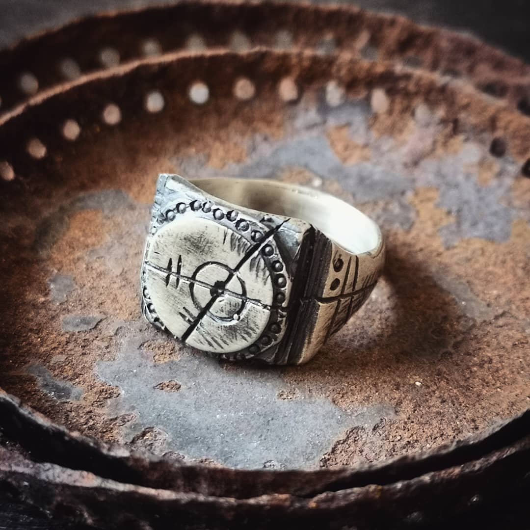 A silver ring with an oxidized and brushed finish, featuring a target design and ornamental details.