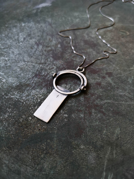A sterling silver necklace with a magnifying glass pendant and a cross on the chain.