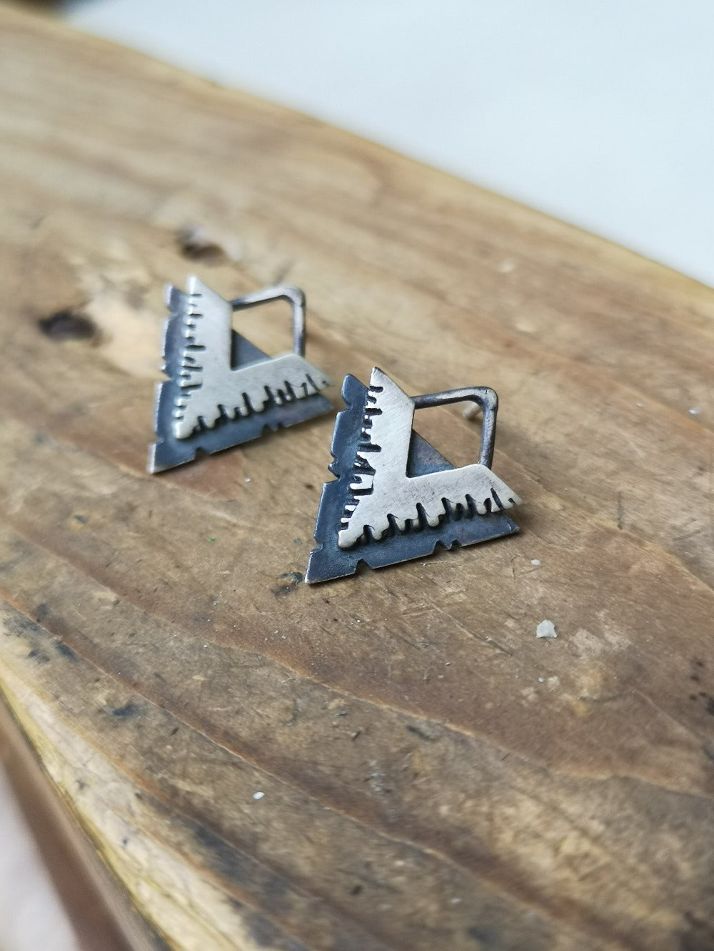 A pair of silver earrings with a geometric design, featuring a triangular shape with lines on the side