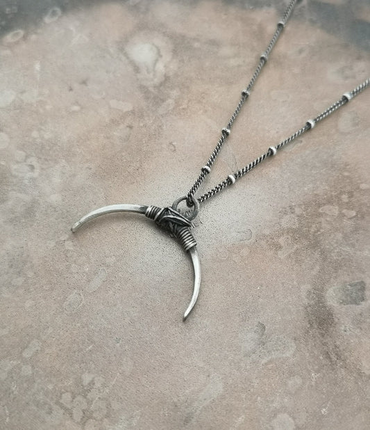 A silver necklace with a crescent-shaped pendant, featuring a chain with a series of small bell-like charms attached to it.