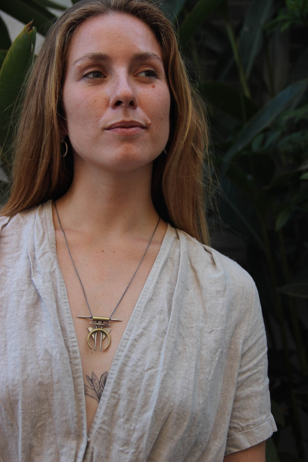 A silver and gold-colored necklace with a geometric pendant, featuring a chain and a series of geometric shaped pendants attached to it.