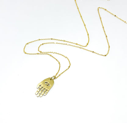 A golden necklace with a white diamond pendant in the shape of Hamsa hand