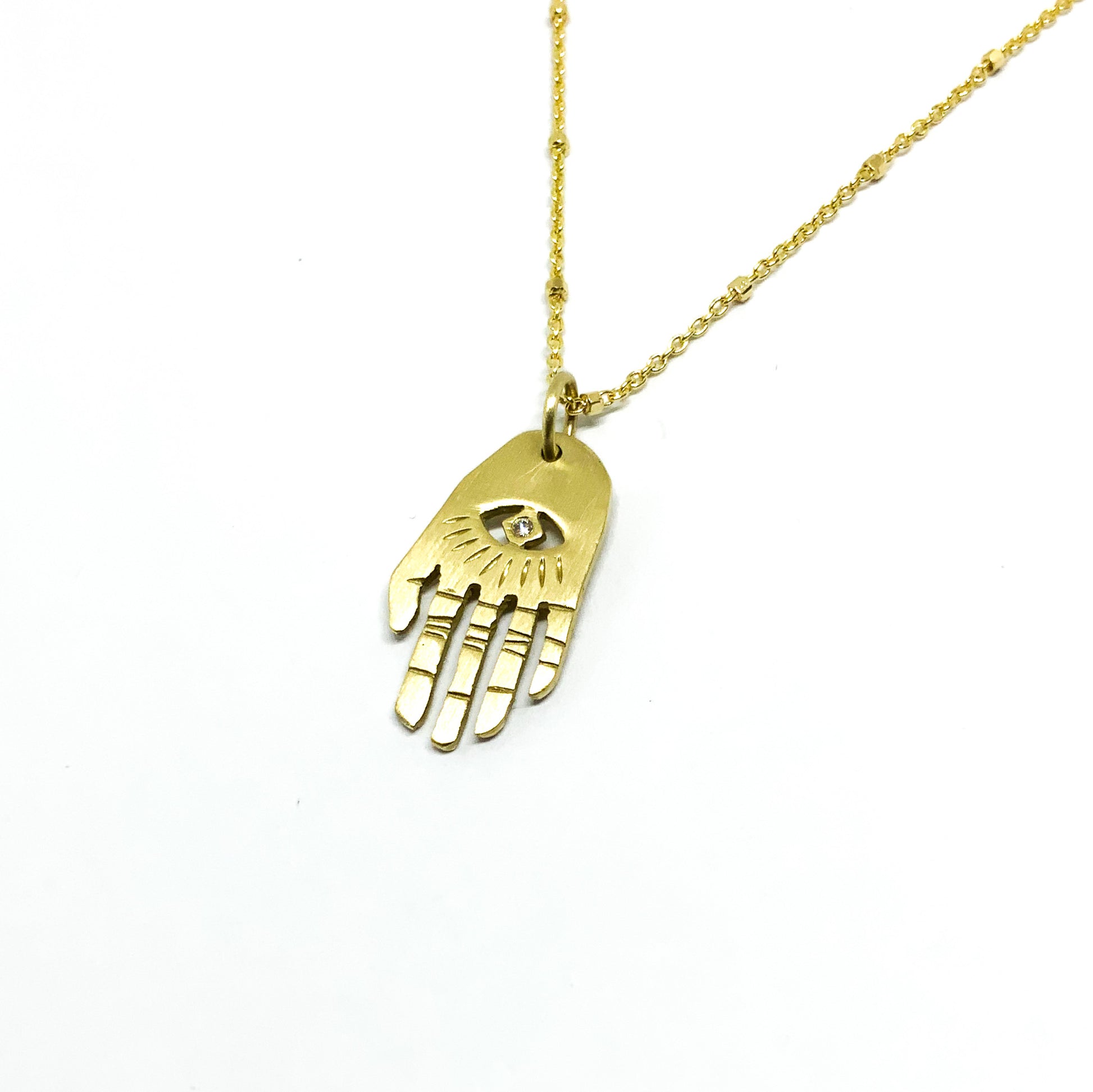 A golden necklace with a white diamond pendant in the shape of Hamsa hand