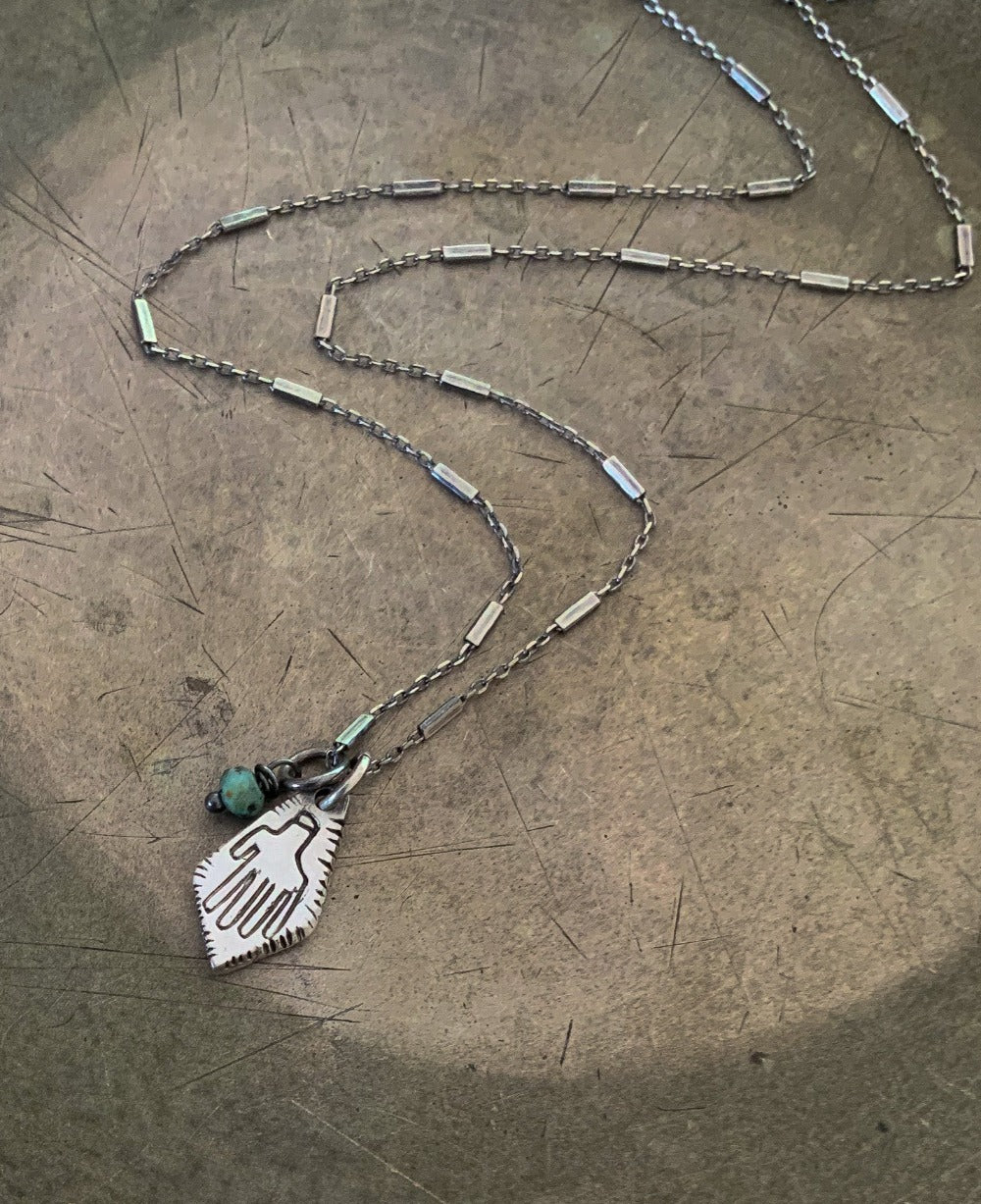 A silver Hamsa necklace with a turquoise stone pendant, featuring a chain and a lobster clasp closure.