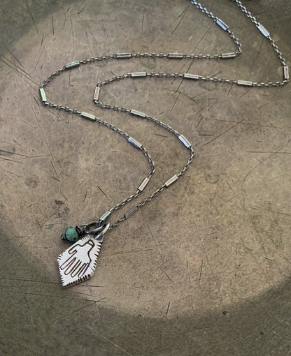 A silver Hamsa necklace with a turquoise stone pendant, featuring a chain and a lobster clasp closure.