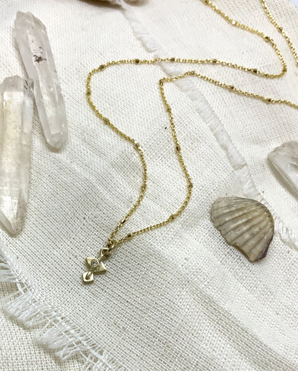 A golden necklace with a white diamond pendant on a textured background 
