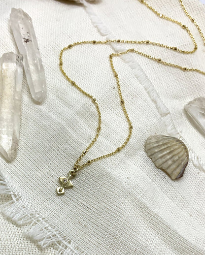 A golden necklace with a white diamond pendant on a textured background 