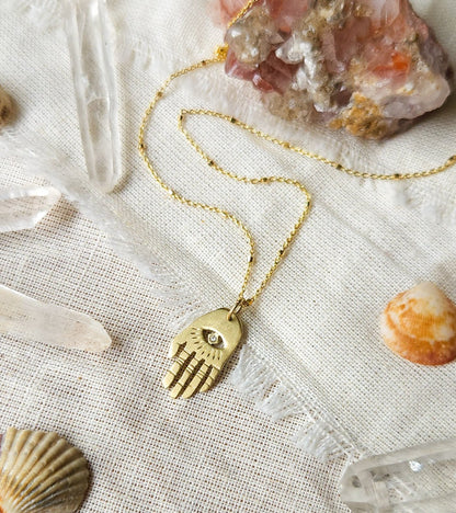 A golden necklace with a white diamond pendant in the shape of Hamsa hand 