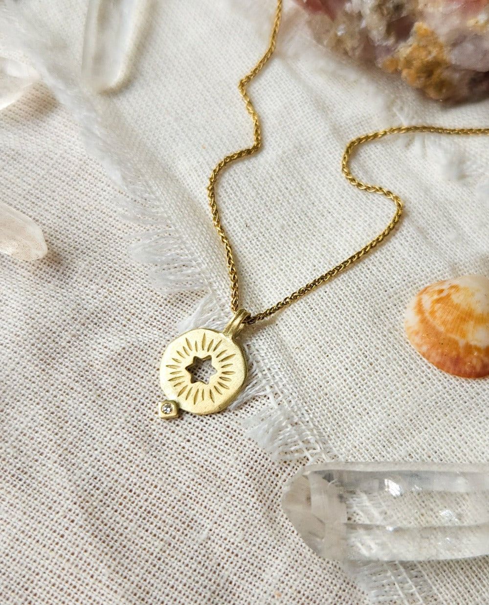 A golden necklace with a white diamond pendant in the shape of a rising star of David, displayed on a lace background with some crystal pieces.