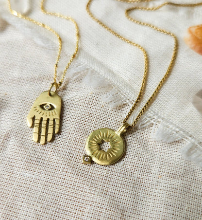 A golden rising star of david pendand on a chain next to golden hamsa hand necklace