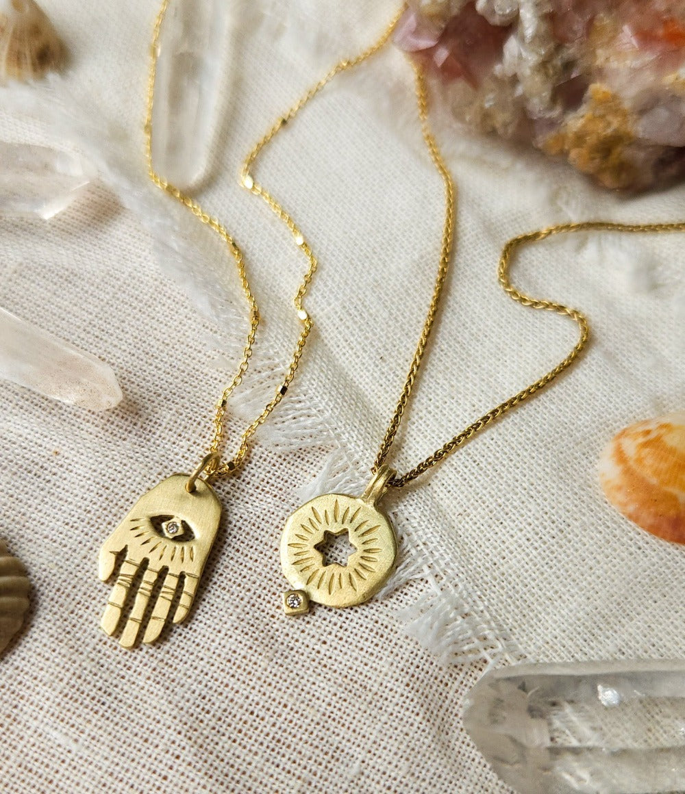 A golden rising star of david pendand on a chain next to golden hamsa hand necklace