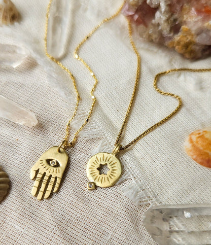 A golden rising star of david pendand on a chain next to golden hamsa hand necklace
