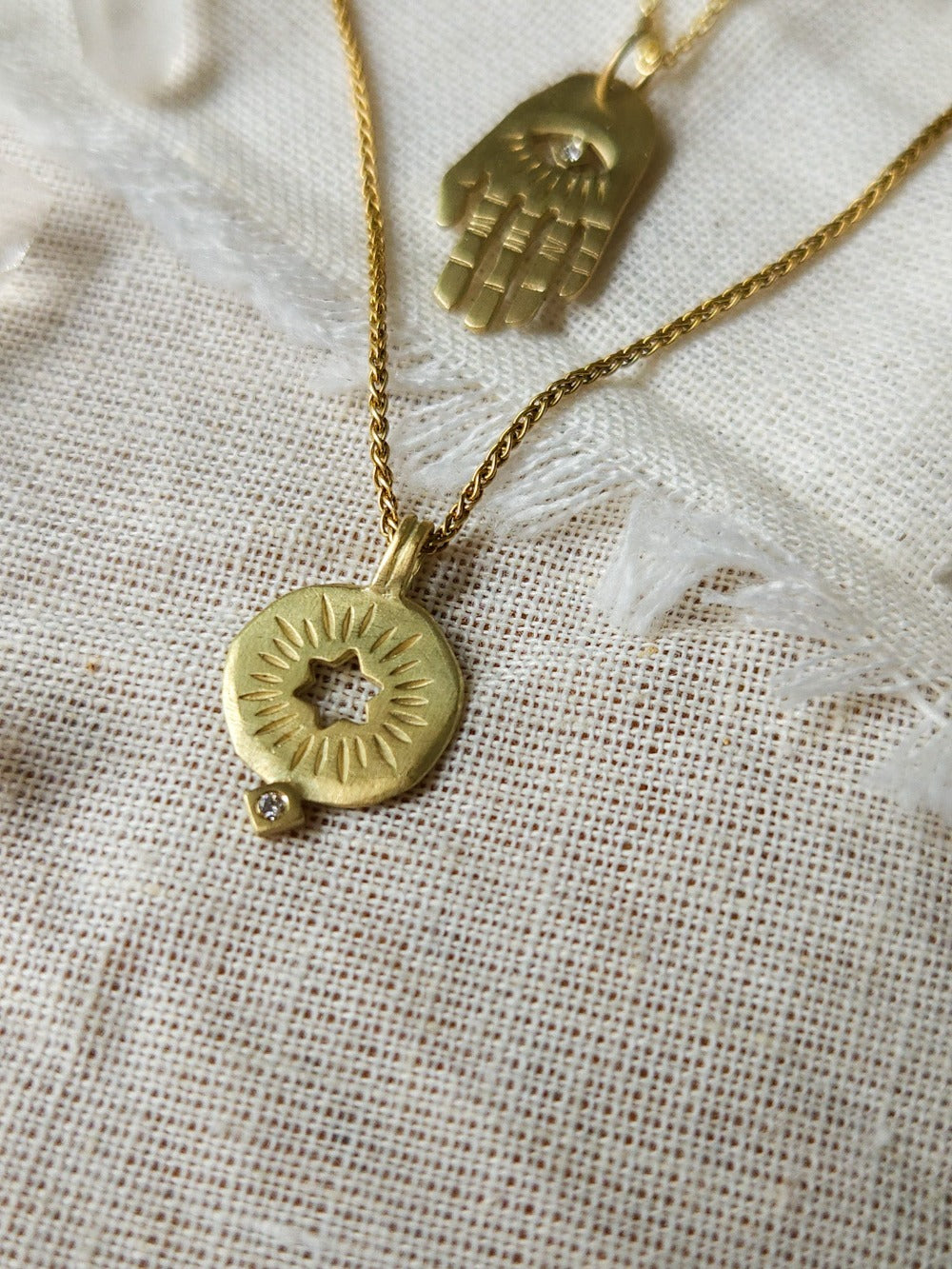 A golden necklace with a white diamond pendant in the shape of a rising star of David, displayed on a lace background with some crystal pieces.