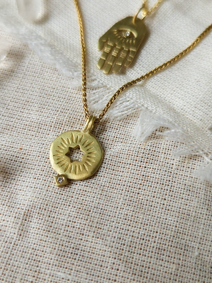 A golden necklace with a white diamond pendant in the shape of a rising star of David, displayed on a lace background with some crystal pieces.