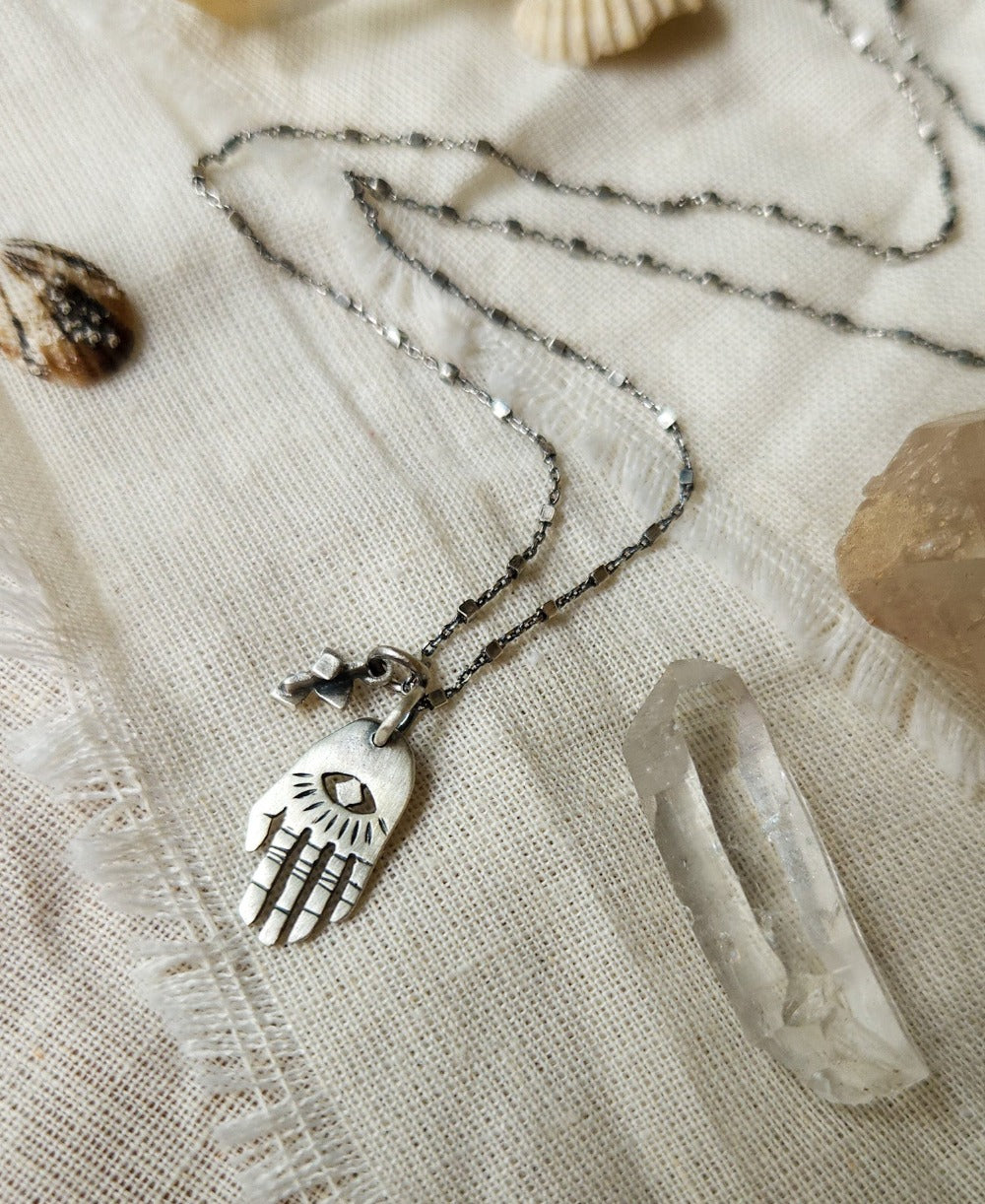 A silver Hamsa necklace with a brushed finish and a chain, featuring a pendant with a Hamsa hand design.