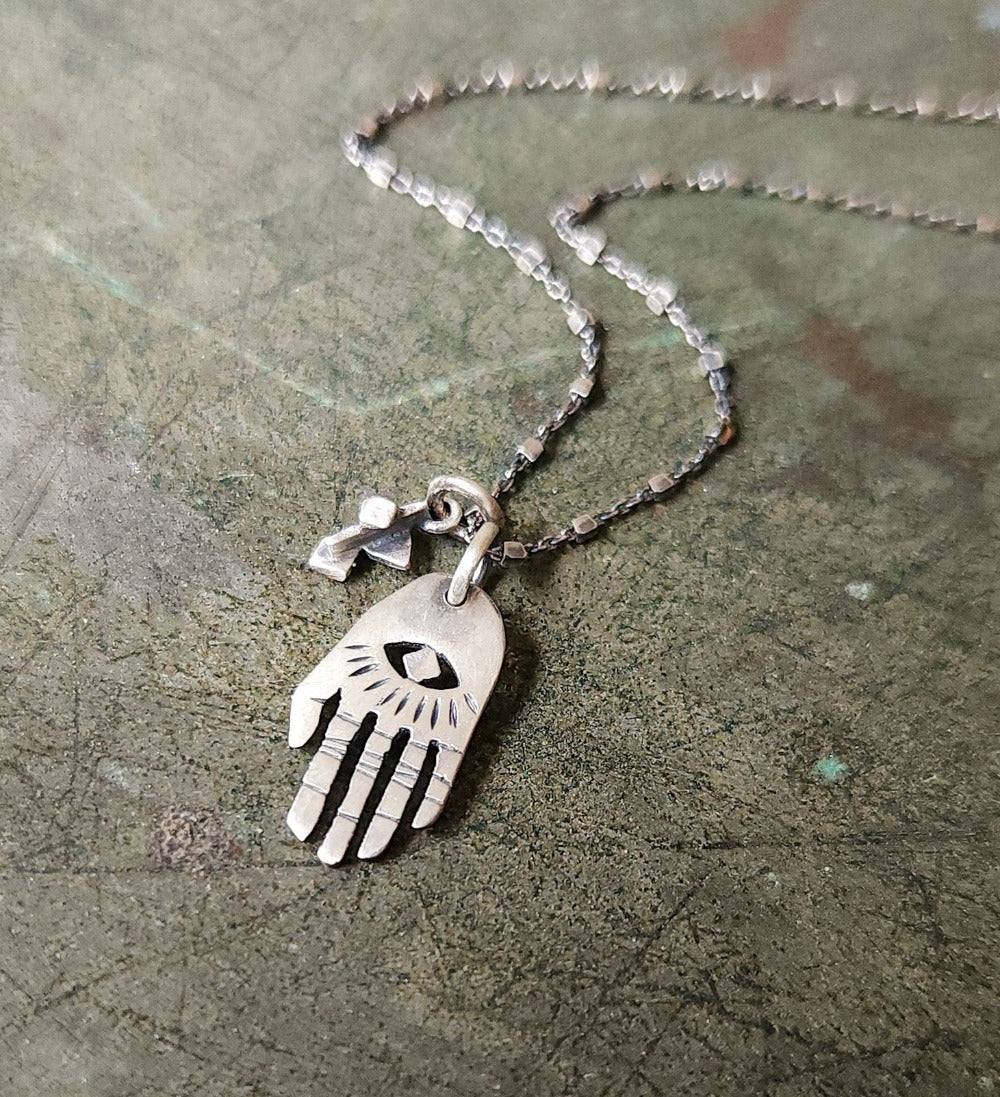 A silver Hamsa necklace with a brushed finish and a chain  featuring a pendant with a Hamsa hand design.