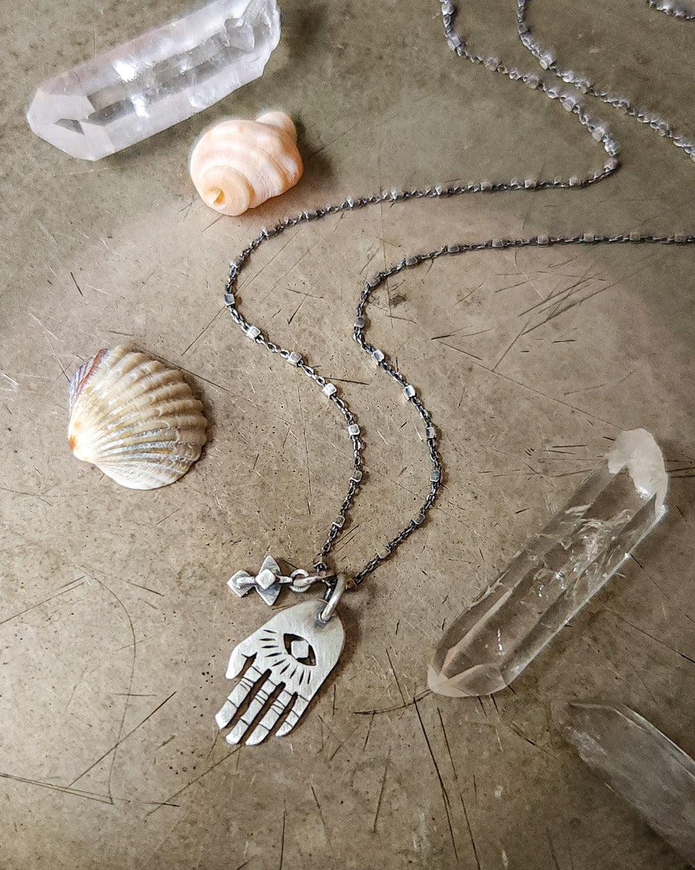 A silver Hamsa necklace with a brushed finish and a chain featuring a pendant with a Hamsa hand design.