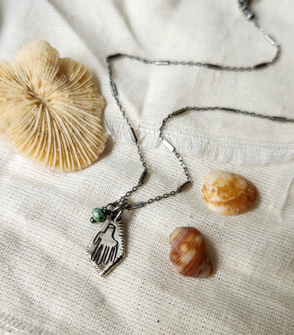 A silver Hamsa necklace with a turquoise stone pendant, featuring a chain and a lobster clasp closure.
