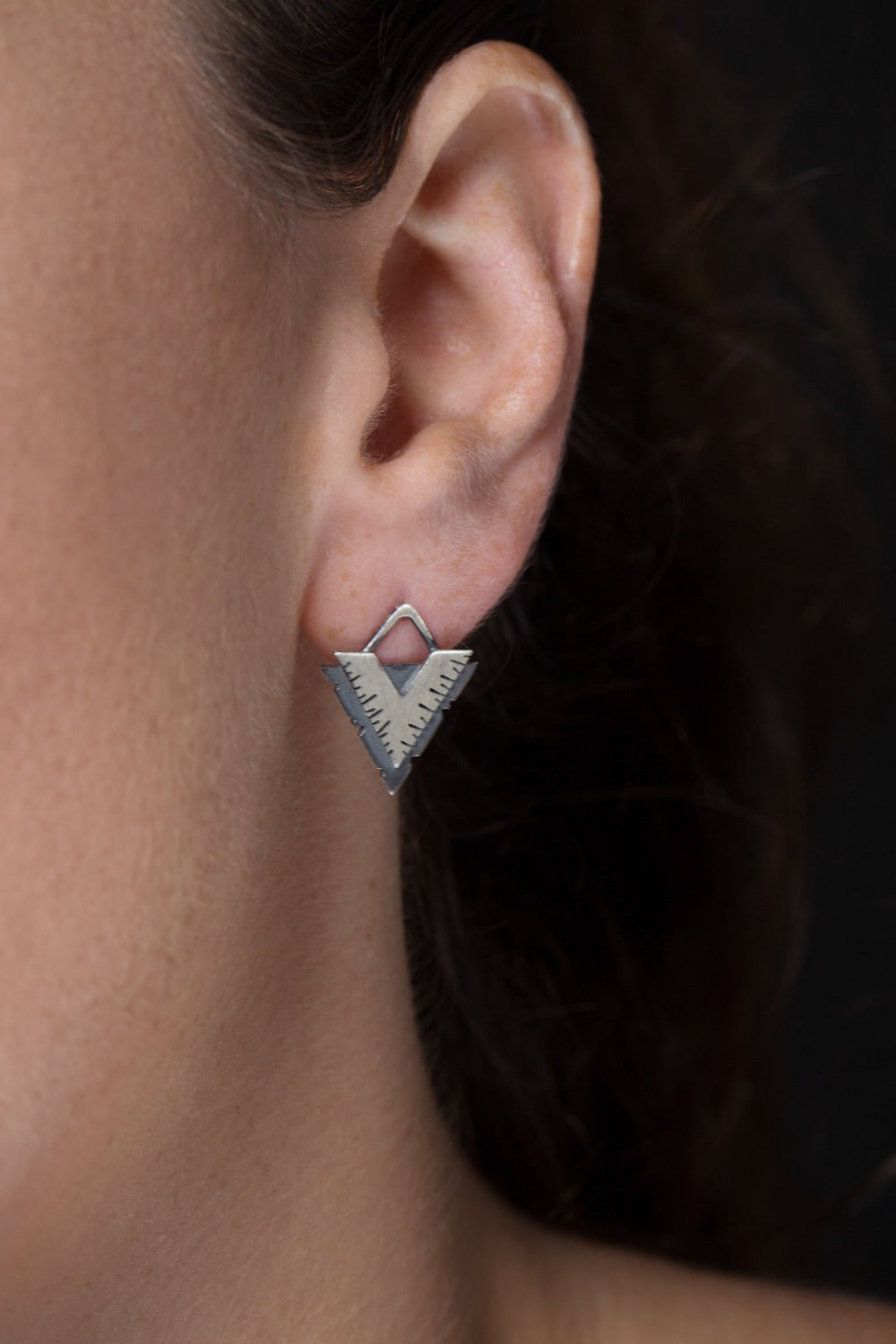 A pair of silver earrings with a geometric design, featuring a triangular shape with lines on the side