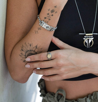 A silver ring with a brushed finish and a central golden brass sun emblem, with engraved patterns around it.