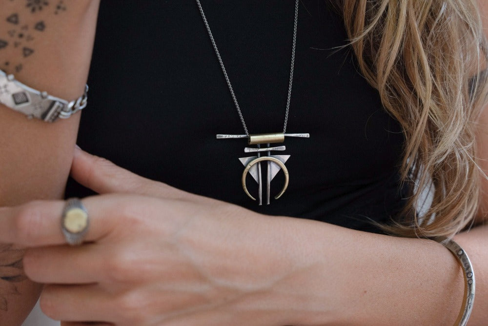 A silver and gold-colored necklace with a geometric pendant, featuring a chain and a series of geometric shaped pendants attached to it.