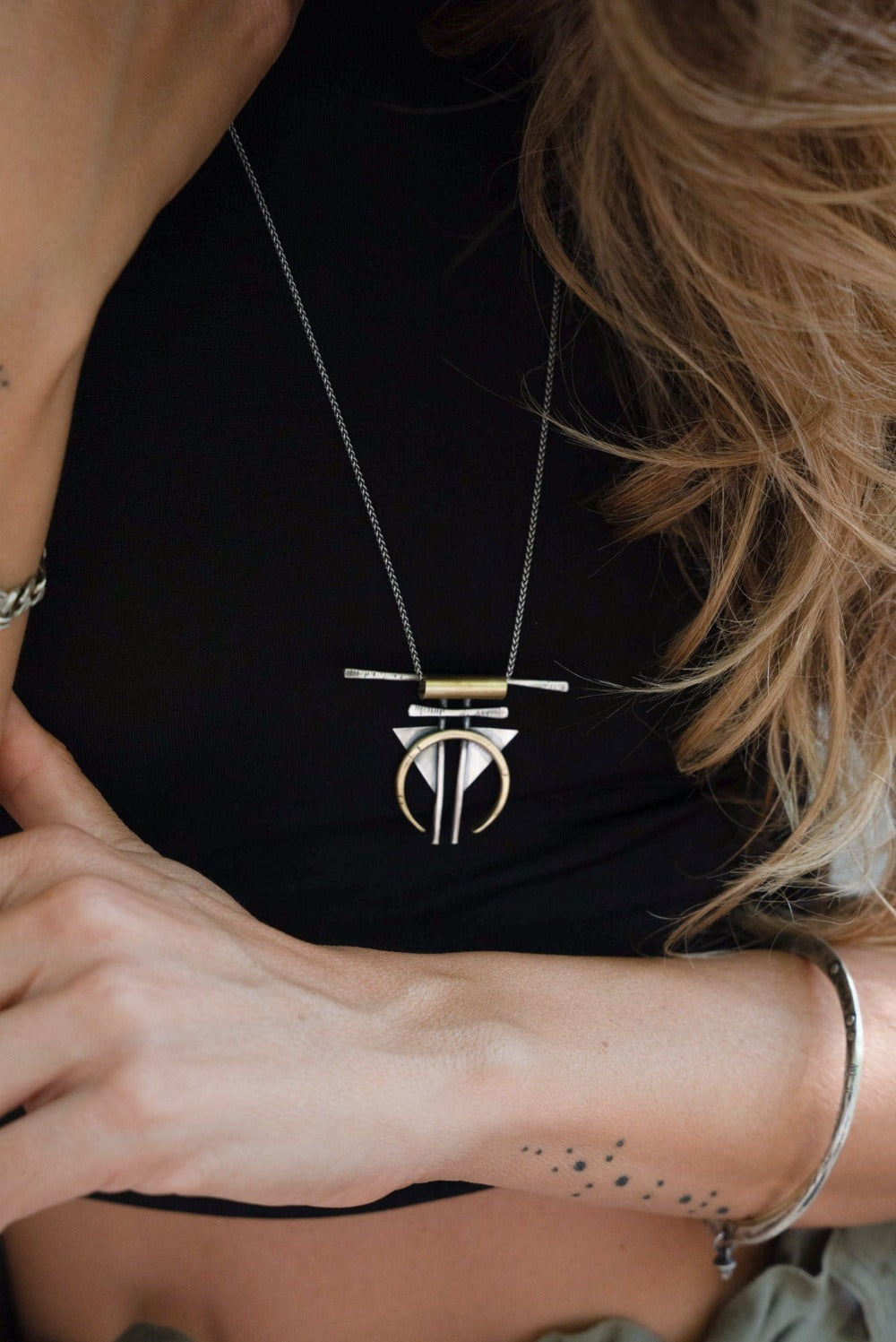A silver and gold-colored necklace with a geometric pendant, featuring a chain and a series of geometric shaped pendants attached to it.