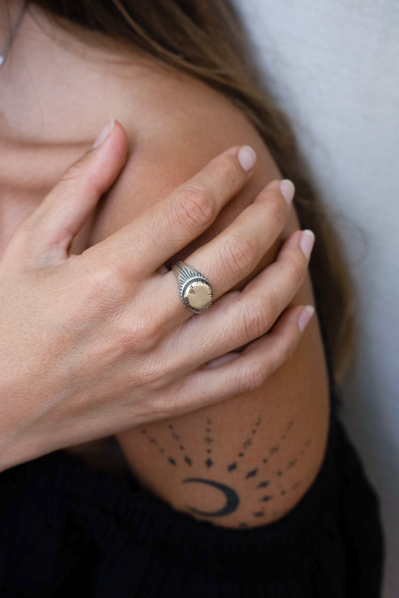 A silver ring with a brushed finish and a central golden brass sun emblem, with engraved patterns around it.