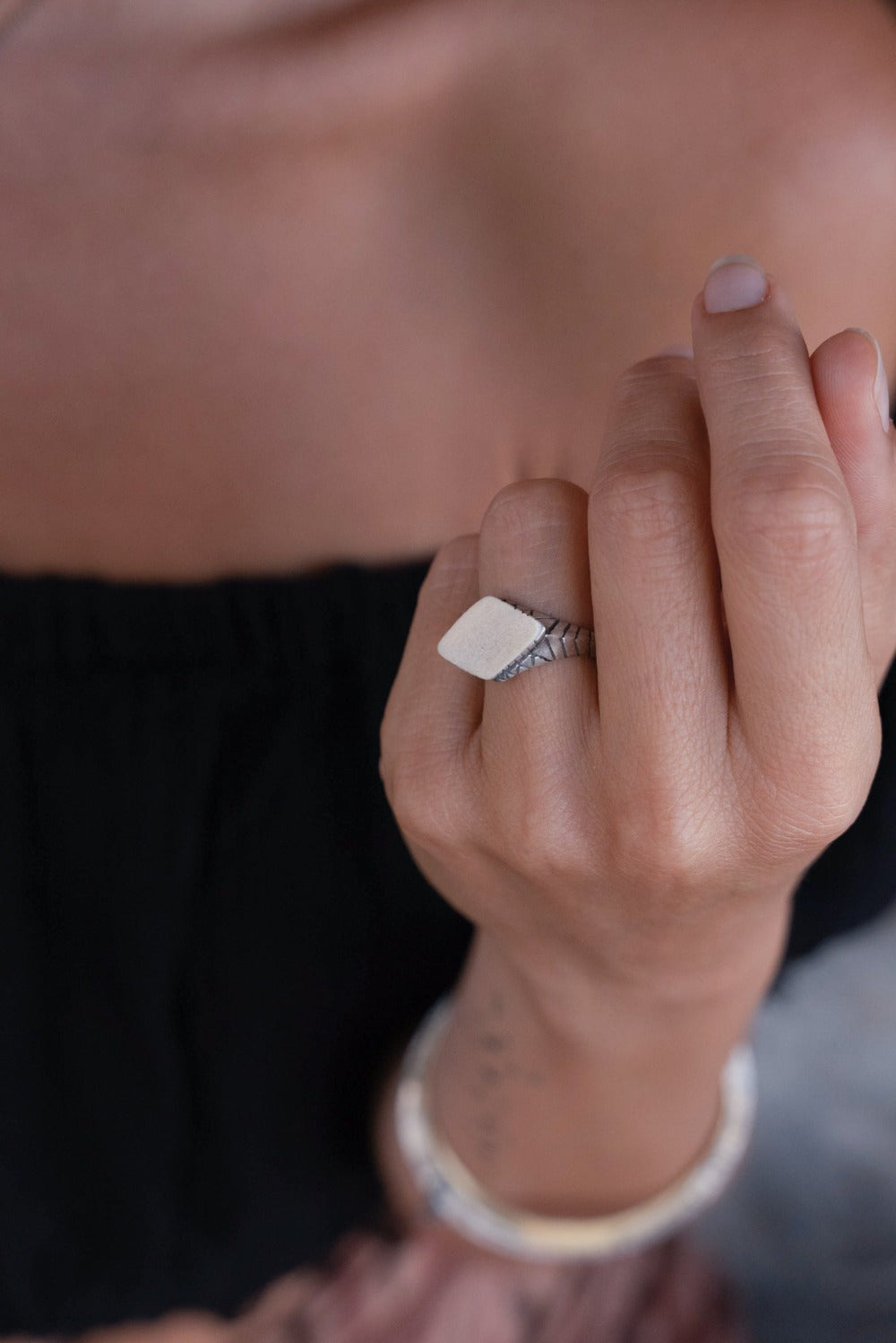 A silver ring with an oxidized and brushed finish, featuring a textured design on the top part.