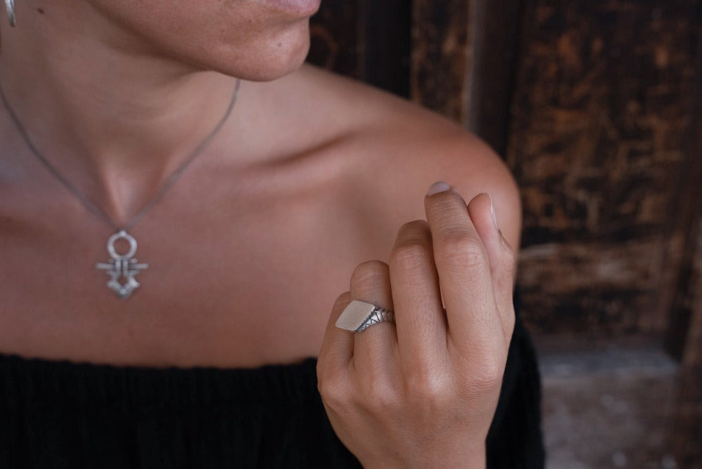 A silver ring with an oxidized and brushed finish, featuring a textured design on the top part.