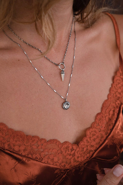 A silver necklace with a pendant featuring a stylized sun and moon design