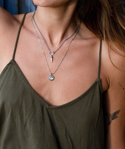 A silver necklace with a pendant featuring a stylized sun and moon design