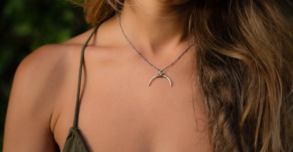 A silver necklace with a crescent-shaped pendant, featuring a chain with a series of small bell-like charms attached to it.