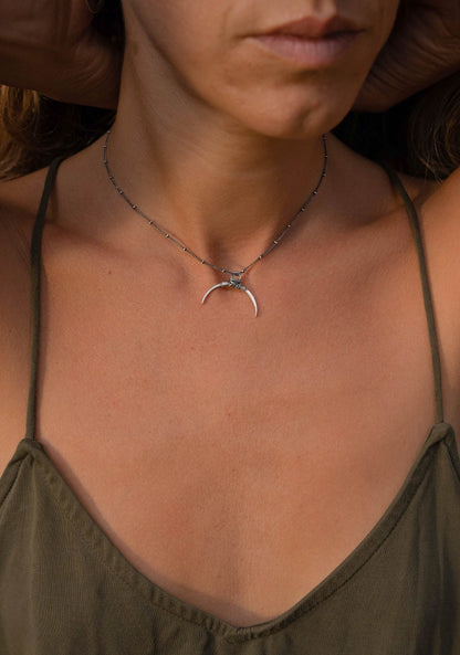 A silver necklace with a crescent-shaped pendant, featuring a chain with a series of small bell-like charms attached to it.