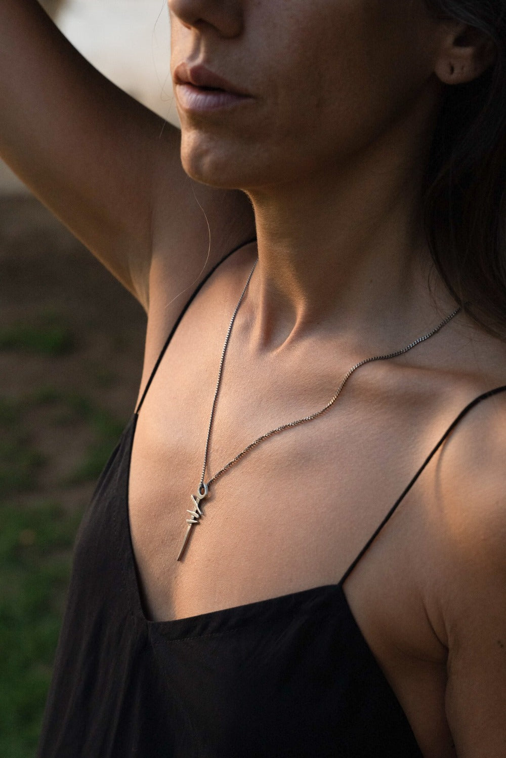 A silver necklace with a pendant featuring a symbol, attached to a chain.