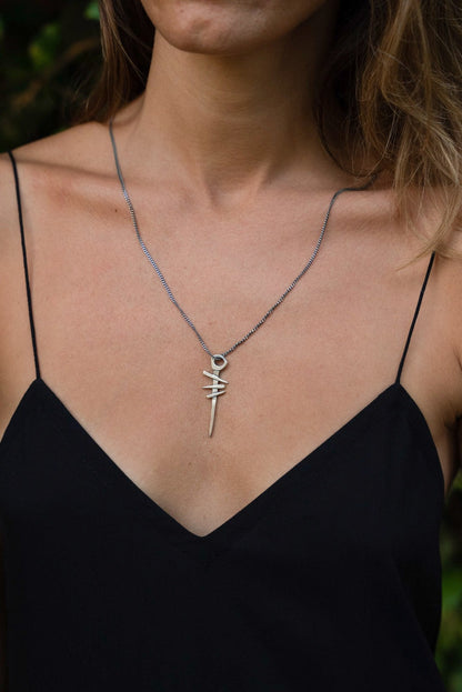 A silver necklace with a pendant featuring a symbol, attached to a chain.