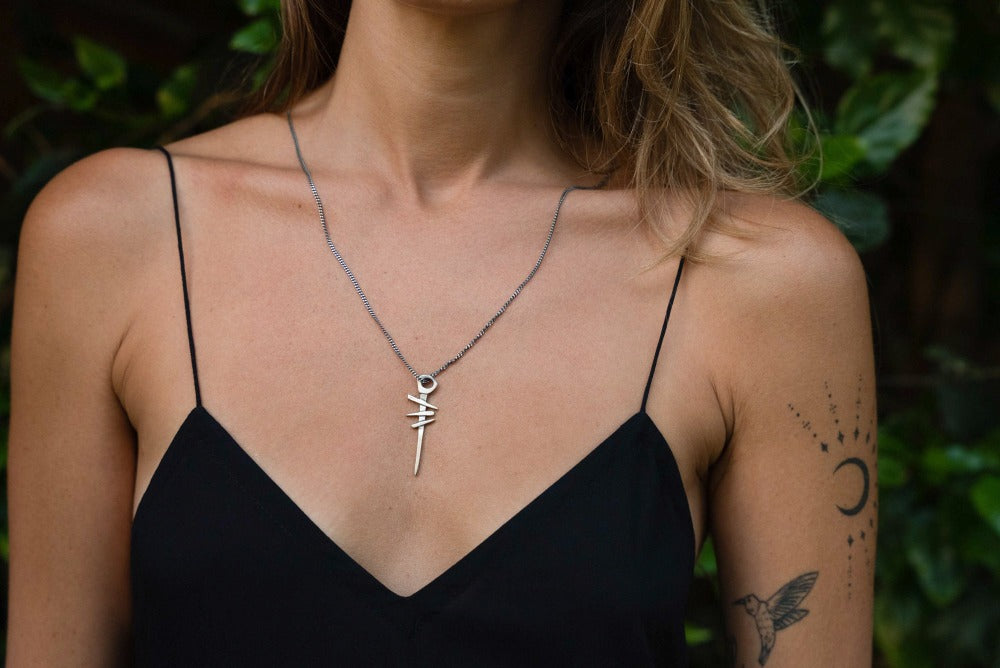 A silver necklace with a pendant featuring a symbol, attached to a chain.