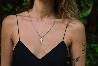 A silver necklace with a pendant featuring a symbol, attached to a chain.
