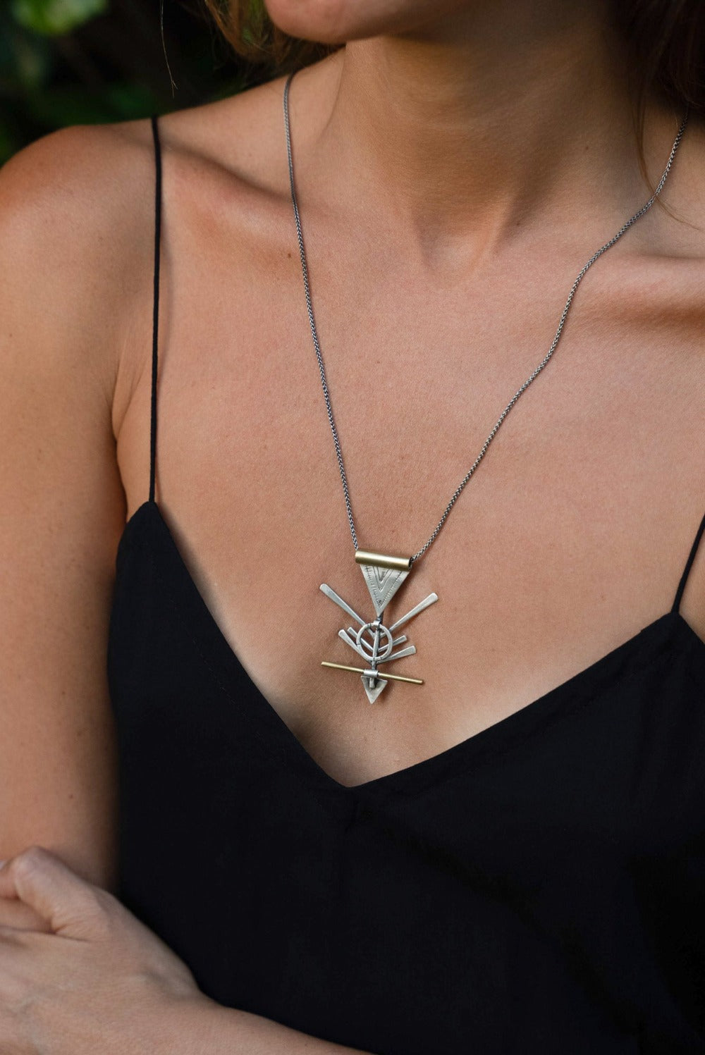 A silver and brass necklace with a geometric pendant, featuring a chain and a series of geometric shaped pendants attached to it.