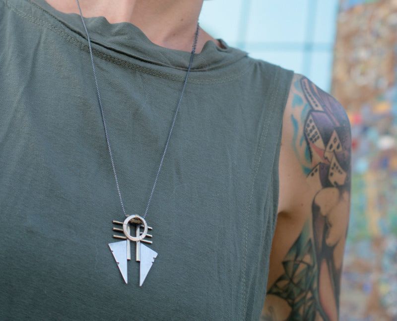 A necklace with a geometric silver pendant featuring a combination of brushed and oxidized finishes, attached to a chain.