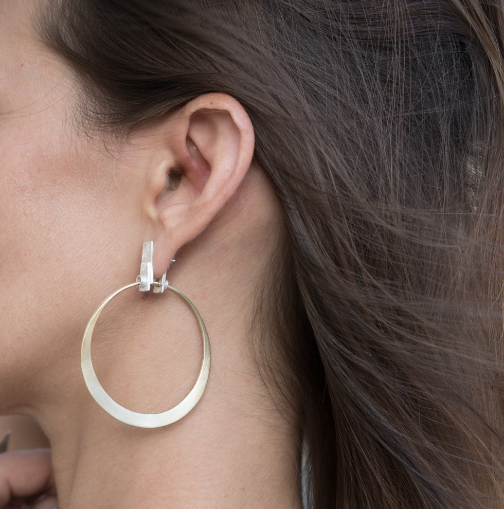 A pair of silver and brass hoop earrings with a brushed finish and a geometric design