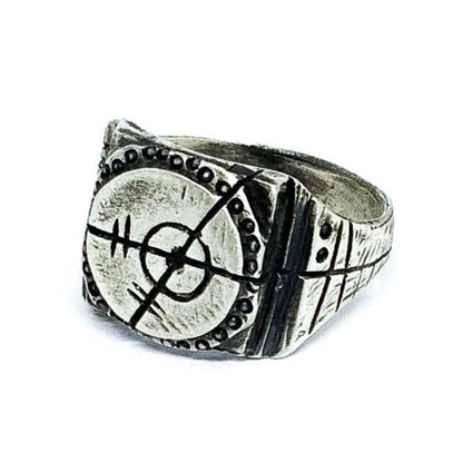 A silver ring with an oxidized and brushed finish, featuring a target design and ornamental details.