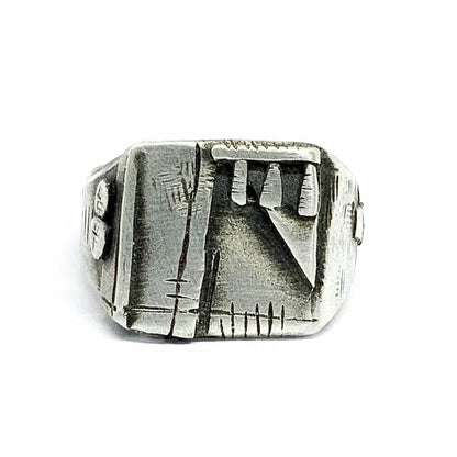 A silver, oxidized and brushed finish ring with a geometric design, signet-style, on a white background.