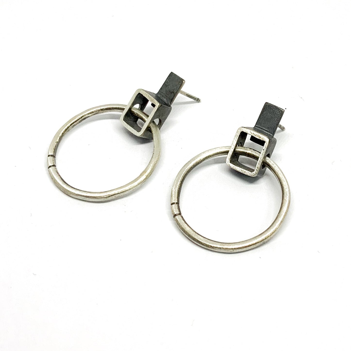 A pair of silver oxidized and brushed finish earrings with a geometric design, displayed against a white background.