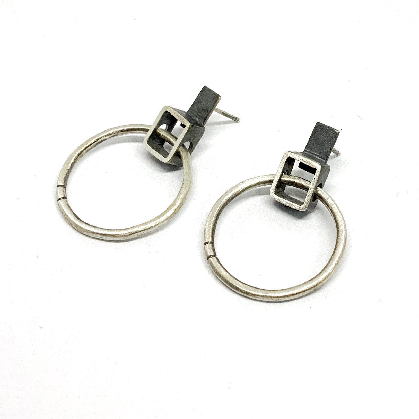 A pair of silver oxidized and brushed finish earrings with a geometric design, displayed against a white background.