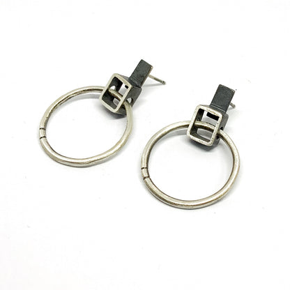 A pair of silver oxidized and brushed finish earrings with a geometric design, displayed against a white background.