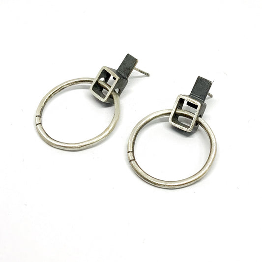 A pair of silver oxidized and brushed finish earrings with a geometric design, displayed against a white background.